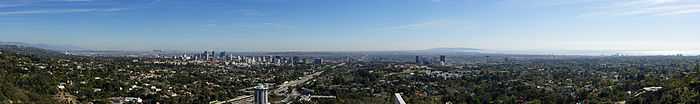 Photo en couleur, prise d'un point élevé, de Los Angeles ; on voit la ville au loin, au premier plan il y a de nombreux espaces verts arborés.