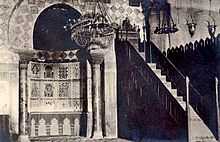 Photographie du mihrab et du minbar d’après une carte postale de 1930. Ce dernier, en bois sculpté, est une chaire à prêcher en forme d’escalier, qui est surmonté d’un siège pour l’imam.