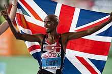 Mo Farah les bras en l'air, un drapeau britannique dans son dos.