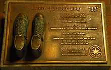 Plaque détaillant les principaux titres et trophées de Bird. Deux chaussures figurent à côté de la description