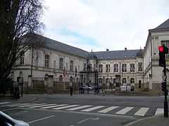 Cour encadrée par trois bâtiments, et fermée par une grille avec portail.