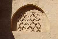 Photographie d’une niche en arc brisé, à fond plat. Ce dernier est orné d’un décor géométrique losangé en briques cuites. L’arc est le vestige d’une ancienne porte murée de la façade occidentale.