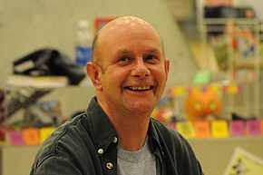 Portrait d'un homme chauve souriant prise dans une librairie.