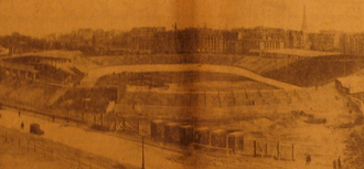 Photo brunie d'un stade vélodrome avec deux tribunes devant des immeubles parisiens.