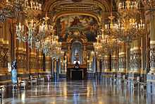 Photo d'une galerie scintillante sous deux alignements de chandeliers, de chaque côté des colonnes et au fond un autel