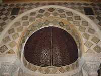 Photographie de la partie supérieure du mihrab. La demi-coupole, coiffant la niche, est réalisée en bois cintré, recouvert d’un enduit épais et peint d’un décor végétal.
