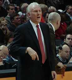 Gregg Popovich en costume, un adjoint dans son dos.