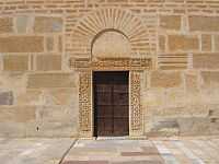Photographie de la porte du minaret, encadrée d’un linteau et de pieds-droits sculptés d’origine antique. Elle est surmontée d’un arc de décharge en fer à cheval.