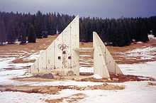 Pièces triangulaires en bois trouées par les coups, avec des anneaux olympiques en partie effacés.