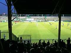 Photographie d'une scène d'un match de football vu des tribunes. Environ une vingtaine de personnes sont sur la pelouse.