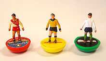 Photo serrée de trois mini-figurines représentant des footballeurs du jeu Subbuteo, une rouge, une jaune et un vert.