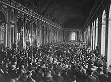 Photographie de la très longue et large Galerie des glaces où une foule innombrable se tient debout autour de personnes assises en groupe sur des chaises.