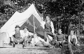 Photo noir et blanc, vers 1907 ; six hommes posent devant une toile de tente installées sous des arbres.